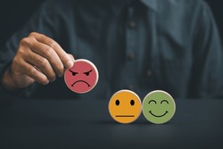 Unsatisfied customer holding frown icon on wooden circle. Conceptual representation of customer satisfaction evaluation, depicting bad experience, negative review, and low score.