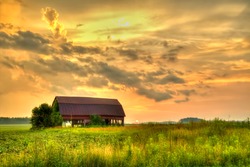 American Midwest Barn Landscape. Sunset over a farm field with a traditional red barn at the horizon.
