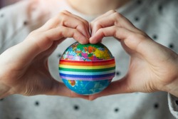 woman's hands in shape of heart holding globe with LGBT rainbow ribbon, lesbian, gay couple and love concept, LGBT marriage 