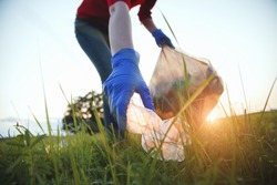 volunteer young woman collecting garbage, picking up waste at sunset light, land pollution, environmental problem