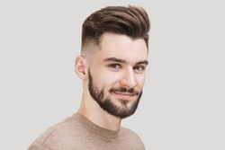 Closeup portrait of handsome smiling young man. Cheerful men isolated on gray background studio shot. Men model face with beard and modern haircut