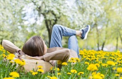 Relaxing woman lying on spring blooming meadow. Girl resting in summer park. Enjoy life, having fun, leisure, relaxation, springtime, lifestyle concept