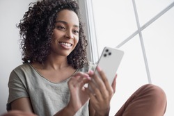 Woman using smartphone at home. Mixed race girl looking at mobile phone. Communication, leisure, connection, mobile apps, technology, lockdown, web chat, lifestyle concept