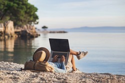 Young woman using laptop computer on a beach. Girl freelancer working by a sea. Freelance work, travel, vacations, stay connected, communication, studying online, e-learning concept