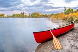 red tandem canoe with a wooden paddle on a lake shore, fall scenery