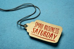 Small Business Saturday sign - a paper price tag with a twine against blue paper background, local holiday shopping concept