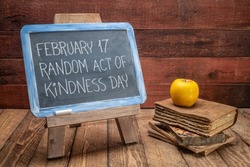 random act of kindness day inspirational reminder  - white chalk handwriting on a vintage slate blackboard with old books against rustic wood background, social concept