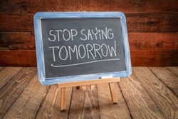 stop saying tomorrow - white chalk handwriting on a slate blackboard, easel sign against rustic, weathered wood, motivation and procrastination  concept