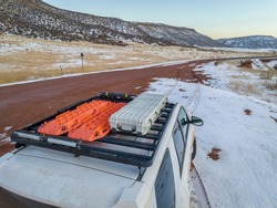 Storage box and recovery ladders on roof racks of SUV driving on a muddy road at Colorado foothills, winter sunset scenery.