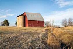 old red barn with twin silo and irrigation ditch at Colorado foothills, winter or early spring scenery at sunset