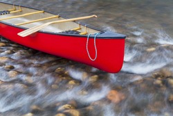 red canoe bow with a rope and paddle against a shallow river rapid