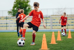 Boy in children's soccer team on training. Kids practicing outdoor with a soccer balls. Training football session for children on soccer camp. Young boy improving dribbling skills. Training with cones