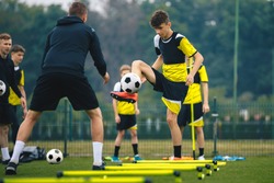 Teenagers on soccer training camp. Boys practice football with young coaches. Junior level athletes improving soccer skills on outdoor training. Player kick soccer ball to coach and ladder skipping
