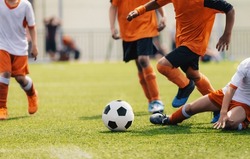 Group of multi-ethnic children playing soccer game. Young boys running after soccer ball on grass football field. Kids in orange and white jersey shirts. The player try to tackle a soccer ball