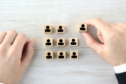 Wooden blocks with human pictogram picked out from employee group by business man's hand
