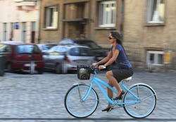 Panning image of a young woman riding her bicycle in a traditional city square.