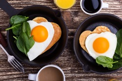 Valentine's day breakfast or brunch. Homemade  heart shape fried egg and pancake in cast iron skillet  with spinach, orange juice and cup of coffee. Table viewed from above