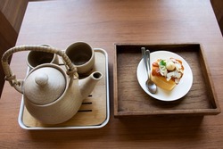 Vintage earthenware tea kettle serve with delicious hazelnut cake topping caramel syrup on wooden tray for thai people eating drinking on tea time in cafe coffee and bakery shop in Bangkok, Thailand