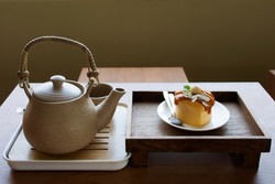 Vintage earthenware tea kettle serve with delicious hazelnut cake topping caramel syrup on wooden tray for thai people eating drinking on tea time in cafe coffee and bakery shop in Bangkok, Thailand