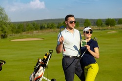 Portrait of young couple golfers are standing together in sportwear and sunglasses, holding golf clubs and happy smiling at gold course. Luxury lifestyle concept.