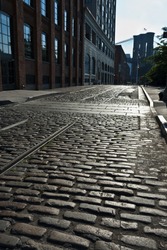 An empty cobblestone street in DUMBO leads to the Brooklyn Bridge in vertical perspective