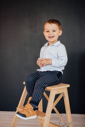 A cute little boy is sitting on a chair. 
