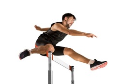 Young male athlete at hurdle race, jumping over the last hurdle. Isolated