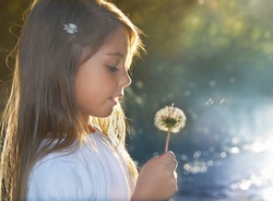 Summer joy, little girl blowing dandelion at sunset near the river