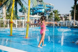 Little girl playing in a swimming pool with fountains in a water park