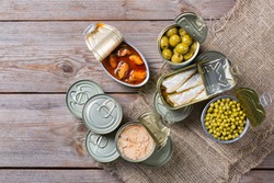 Assortment of different canned preserved vegetables, meat, fish, seafood in tin cans on a wooden table. Non-Perishable goods, food, donations concept. Flat lay top view background 