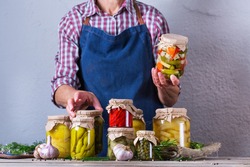 Senior mature woman holding in hands jar with homemade preserved and fermented food. Variety of pickled and marinated vegetables. Housekeeping, home economics, harvest preservation  