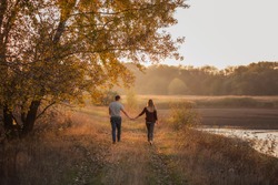 A young man and a girl are walking  in the autumn forest next to the lake. Couple in love  spend time forever together. Traveling during the cold season, on weekend days. Happy lovers hold hands, kiss