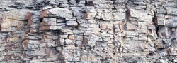 Rock cliff face background. Dangerous vertical wall with protruding crumbling layered stone blocks in quarry for the extraction of wild stone. Abstract texture for stone mining industry