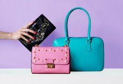Colourful bags purses on purple background. Woman hand with red manicured nails holding wallet.