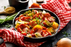 Stew with peppers and sausage in a cast iron skillet on a black background, close up. Traditional Hungarian dish called lecho