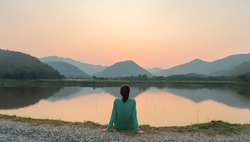 Social distancing, a woman is sitting alone by the lake during sunset moment.
