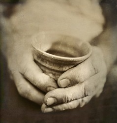 Vintage Style Photo of Man's Worn Hands Holding Cracked Japanese Ceramic Cup. Artistic treatment with texture, toning and grain added for effect. Concept of age, experience and the passing of time.
