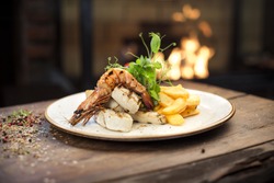 Food - Main course gourmet seafood - Delicious grilled king prawn with chicken fillet and homemade french fries served on a wooden table, fireplace on background