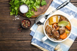 Close-up of slow cooked meat stew ragout in bowl with beef, potato, carrot, broth on wooden rustic background, top view with space for text. Hot homemade food for dinner, meat casserole copy space