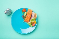 Intermittent fasting low carb hight fats diet concept flat lay, healthy food salmon fish, bacon meat, vegetables and salad on blue plate and clock alarm on blue background top view, space for text