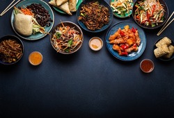 Set of Chinese dishes on table: sweet and sour chicken, fried spring rolls, noodles, rice, steamed buns with bbq glazed pork, Asian style banquet or buffet, top view with copy space