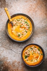 Two ceramic bowls with pumpkin cream soup decorated with peanuts on rustic old metal oven tray background with spoon, from above. Autumn cozy dinner concept 