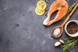 Fresh raw salmon steak, lemon, herbs, spices, wooden spoon on dark rustic concrete background. Food frame. Ingredients set for making healthy dinner. Healthy/diet concept. Space for text. Fresh fish  