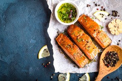 Delicious fried salmon fillet, seasonings on blue rustic concrete background. Cooked salmon steak with pepper, herbs, lemon, garlic, olive oil, spoon. Space for text. Fish for dinner. Healthy eating