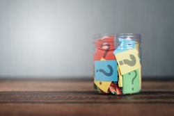 colorful paper with question mark in a plastic jar on wooden table. questions and diversity concept. FAQ and Q&A background concept