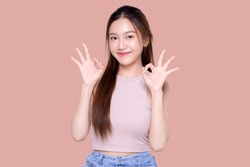 Beautiful young Asian woman with healthy and perfect skin hows OK signal on isolated pink background. Facial and skin care concept for commercial advertising.