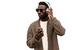 Portrait stylish african man with smartphone in wireless headphones listening to music looking away wearing brown knitted cardigan and sunglasses isolated on white background
