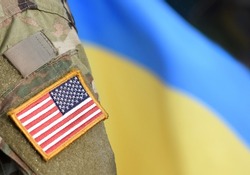 American Flag on Soldiers arm and flag of the Ukraine at background. US military support Ukraine.