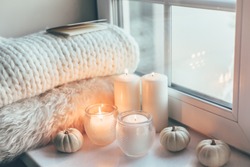 Warm and cosy hygge concept with white sweater and candles on a windowsill