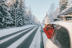 Rear view of teen girl in car over snowy forest on winter roadtrip to the nordic way
